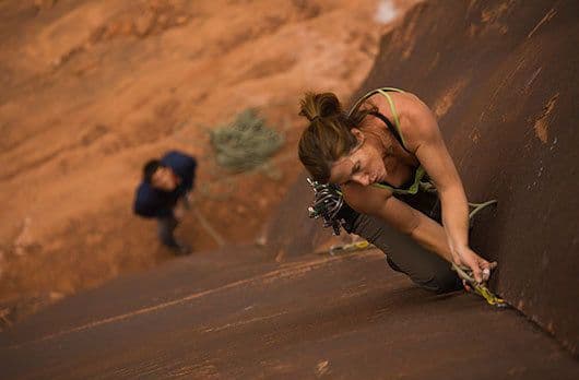 Woman climbing in Moab with assistance of a partner 