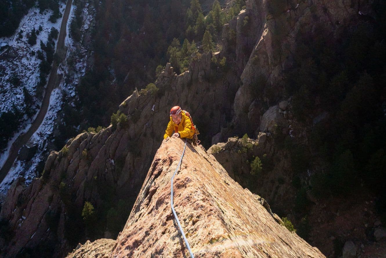 A climber ascends down a steep and narrow cliff
