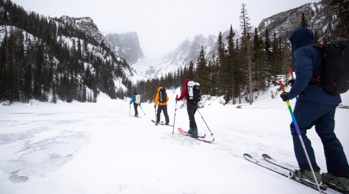 Four skiers skin across a frozen lake in Rocky Mountain National Park.