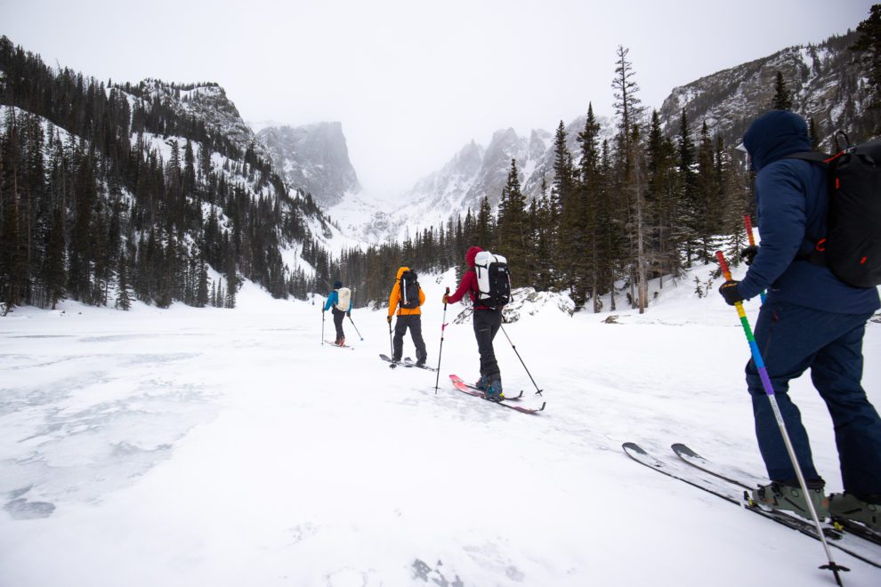 Four skiers skin across a frozen lake in Rocky Mountain National Park.