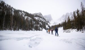 Four skiers skin across a lake in Rocky Mountain National Park.