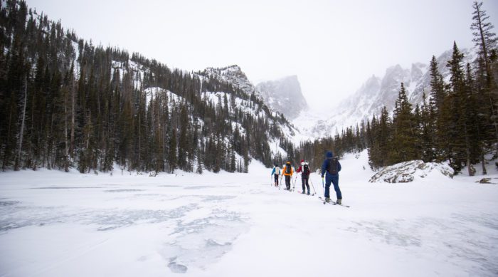 Four skiers skin across a lake in Rocky Mountain National Park.