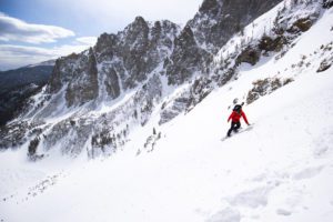 Snowboarder in a red jacket descends down a slope in Rocky Mountain National Park.