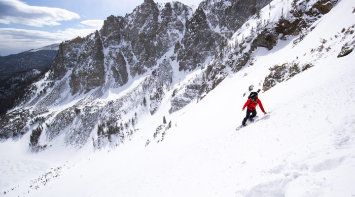 Snowboarder in a red jacket descends down a slope in Rocky Mountain National Park.