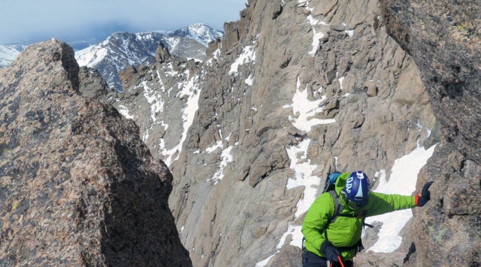 a climber in green jacket climbing a mountain