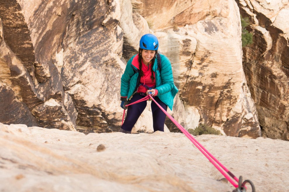 A woman in a blue helmet repelling at Red Rocks.