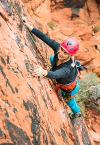 A woman in a pink helmet top rope climing on sandstone rock.