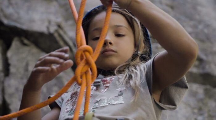 A young girl learns how to tie into her climbing rope.
