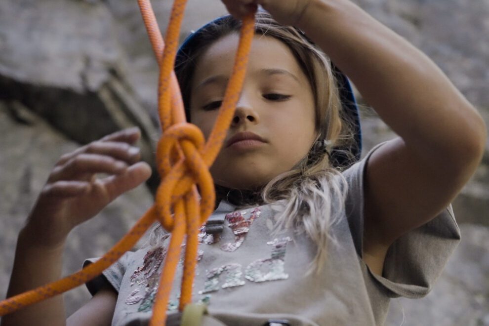 A young girl learns how to tie into her climbing rope.