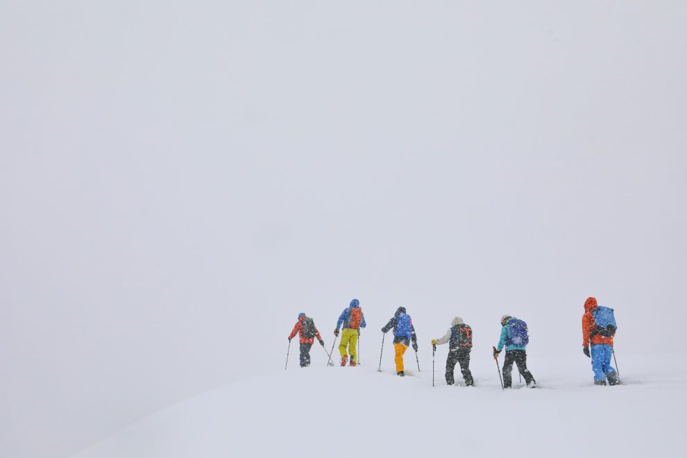 Six skiers skinning on a stormy, grey day.