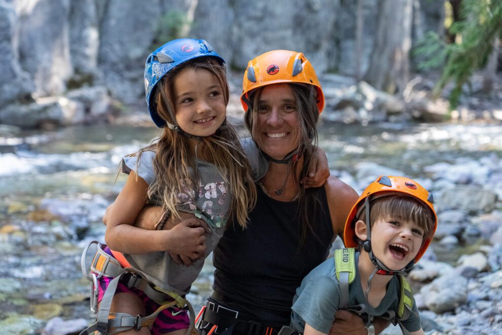 Two kids and their mother smile on a rock climbing adventure.