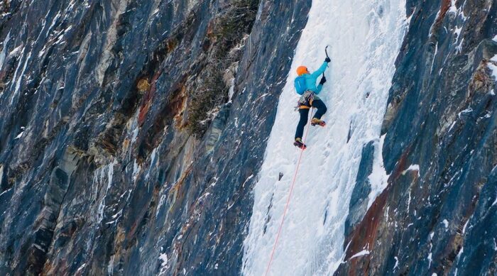 Lead climber ice climbing in a blue jacket.