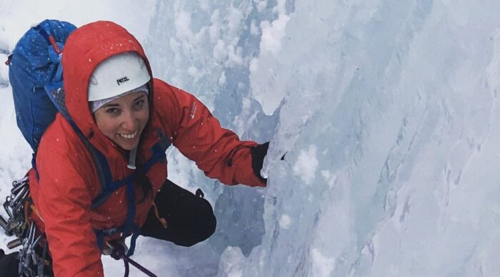 A smiling female in a red jacket ice climbing.