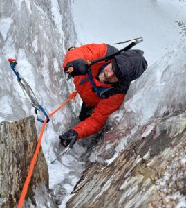 Male in a red jacket ice climbing on top rope.