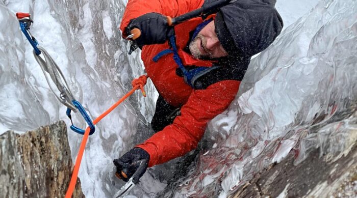 Male in a red jacket ice climbing on top rope.