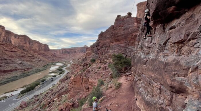 A climber and belayer climb in a river canyon in Moab, Utah.