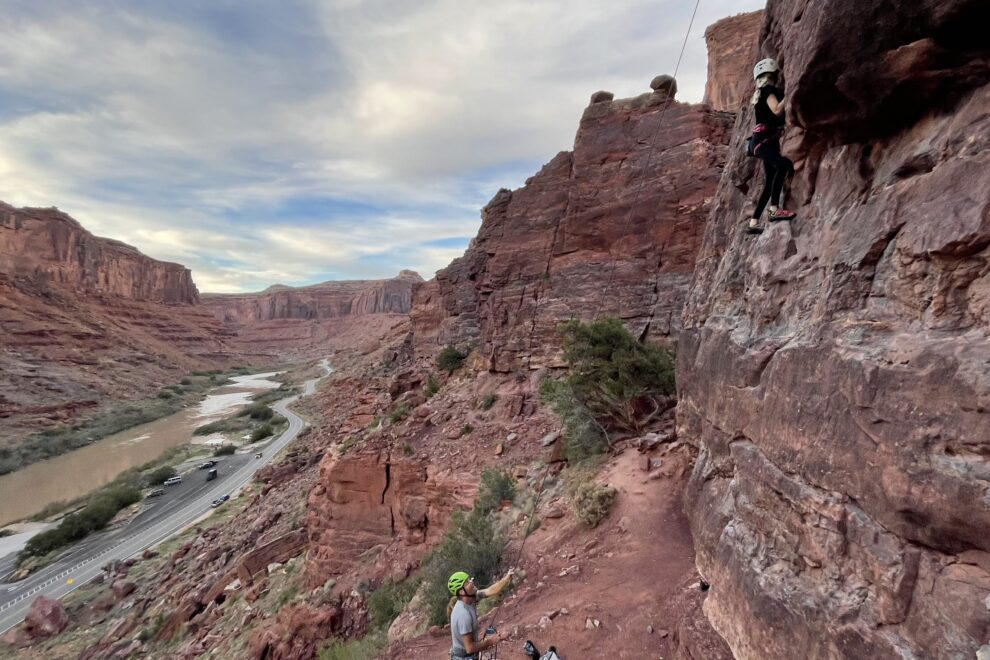 A climber and belayer climb in a river canyon in Moab, Utah.