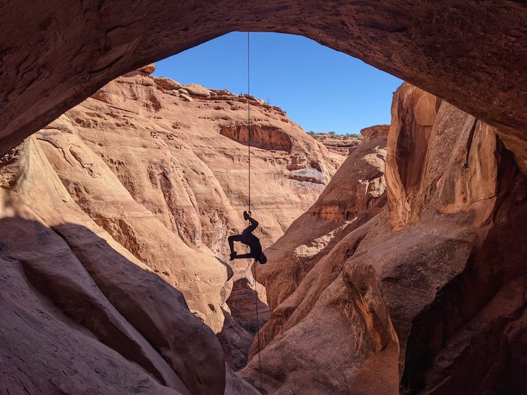 A female strikes an acrobatic pose while rappelling from an archway in Moab, Utah.