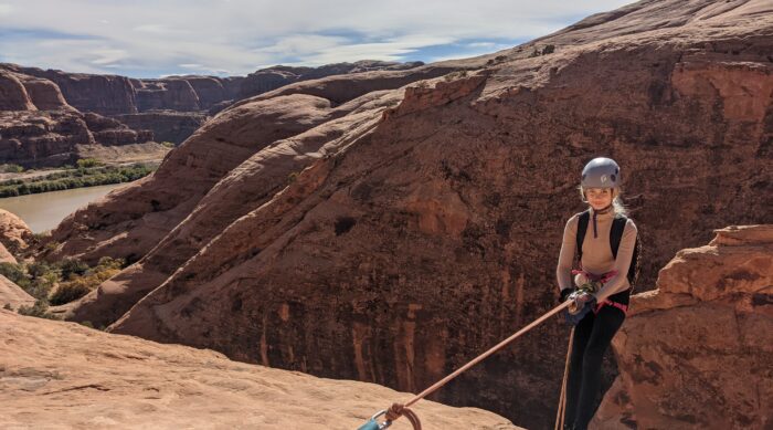 A girl in a brown helmet rappels off a sandstone rock in Moab, Utah.