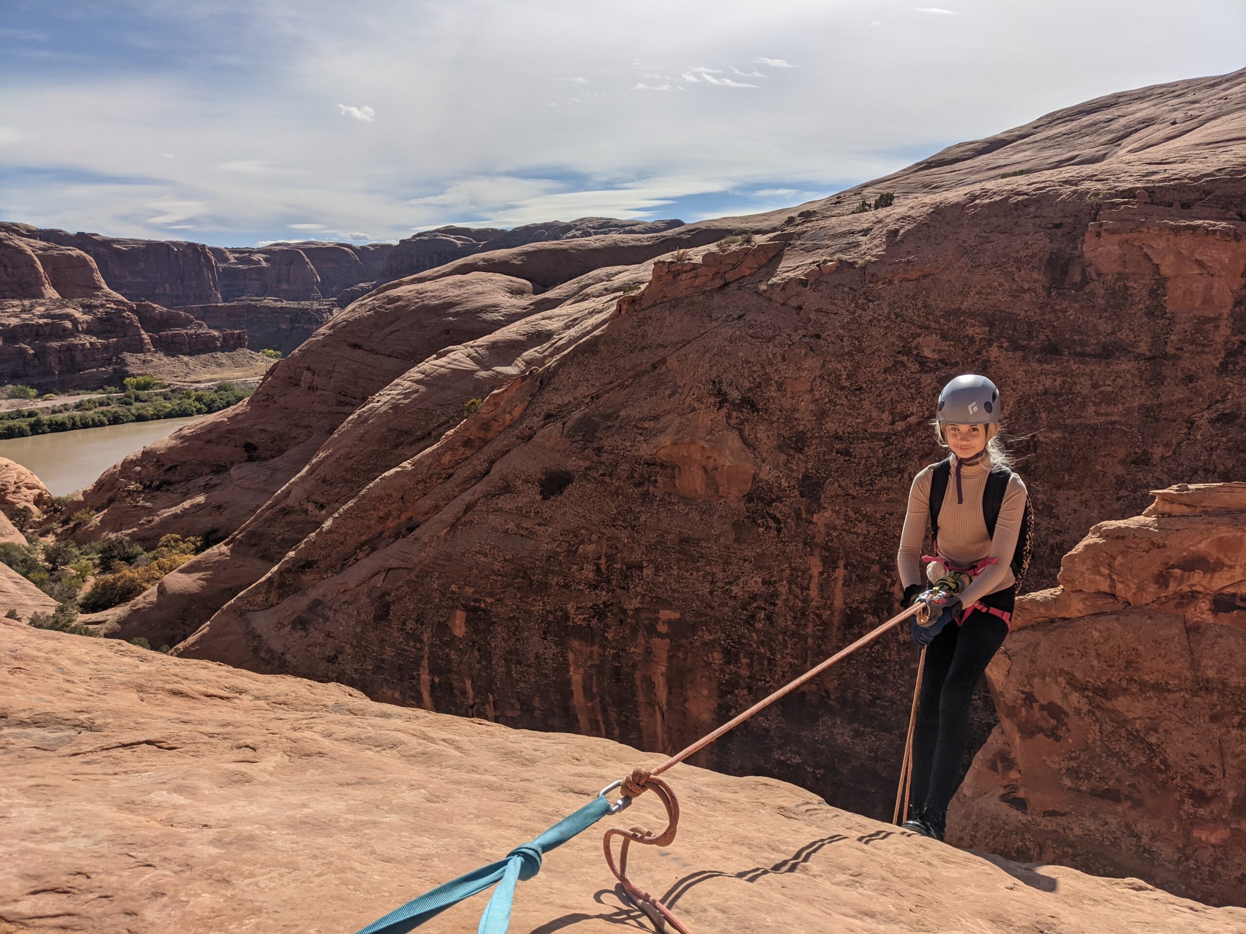 A girl in a brown helmet rappels off a sandstone rock in Moab, Utah.