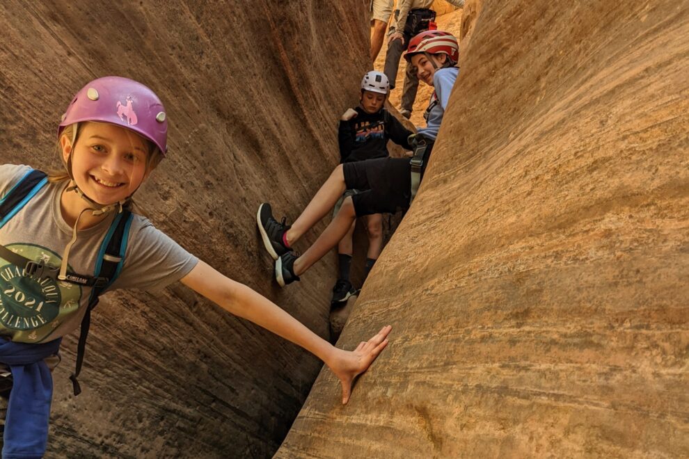 A young girl in a purple helmet climbs through a sandstone canyon.