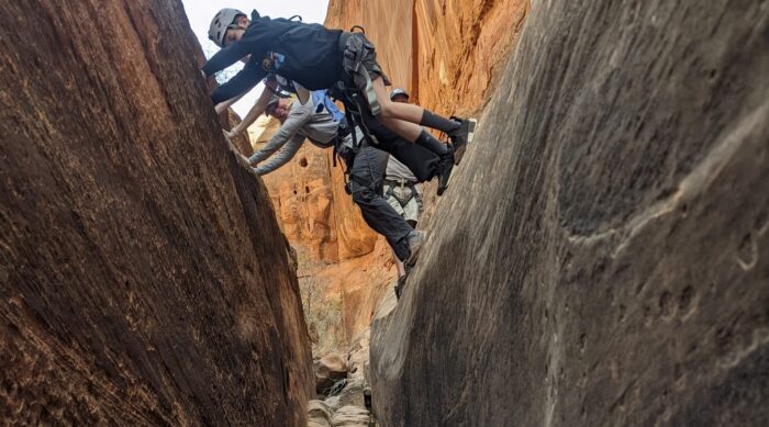 Two clients shimmy through a sandstone canyon.