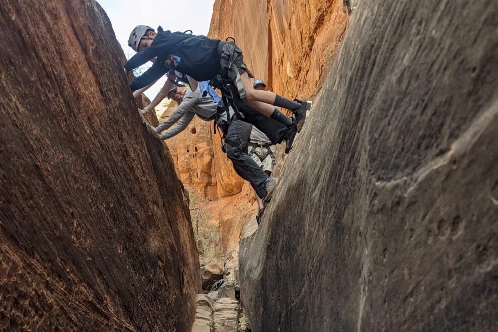 Two clients shimmy through a sandstone canyon.