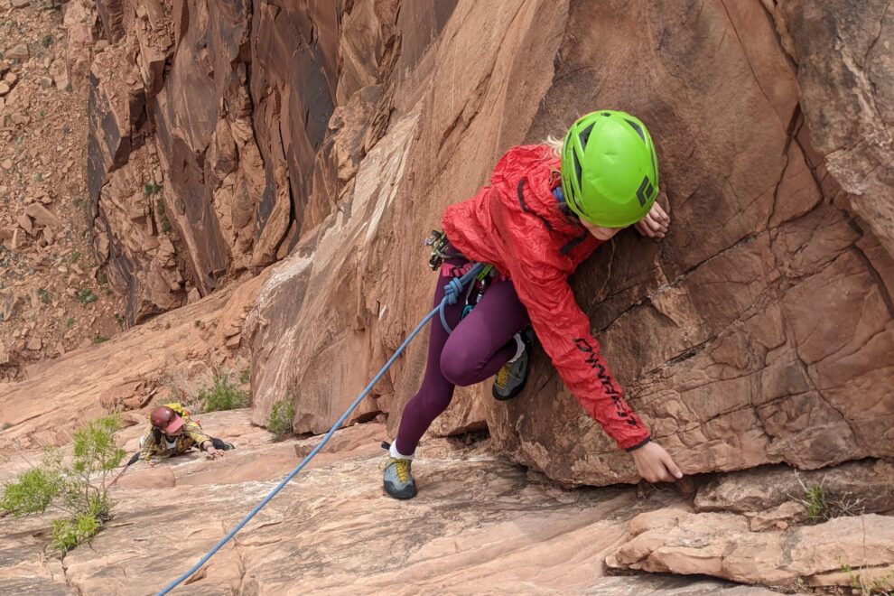 A climber in a red jacket lead climbs up a sandstone crack in Moab, Utah.